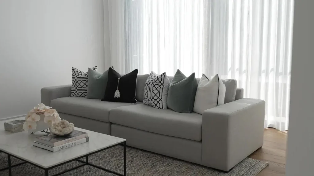 Sofá gris con cojines en tonos neutros y verdes, mostrando un ejemplo moderno y equilibrado que ayuda a entender mejor cómo elegir cojines para el sofá de tu salón según el estilo de la casa